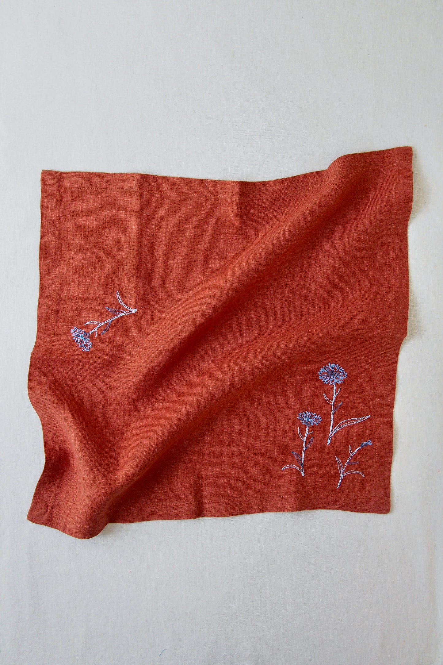 Rust linen napkin with blue embroidered flower detail